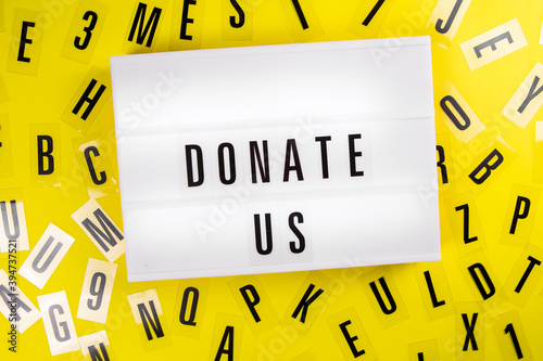 Donate Us message on lightbox on scattered letters background of plastic alphabet. charitable foundation, call for donations, compassion, money transfers to charity organizations, philanthropy concept