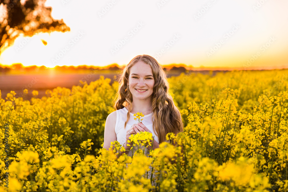 Teenage girl in field of canola on farm at sunset smiling Teenage girl in field of canola on farm at sunset smiling