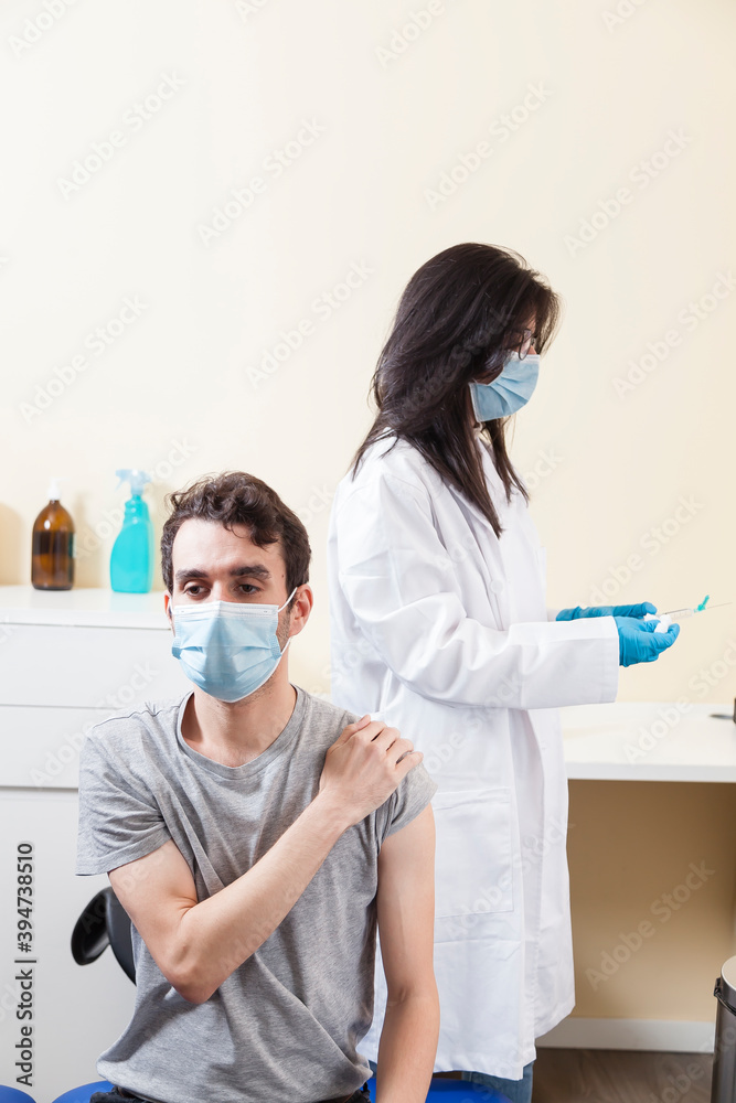 Vertical shot of man wearing surgical mask waiting for the doctor to vaccine him on a clinic. 