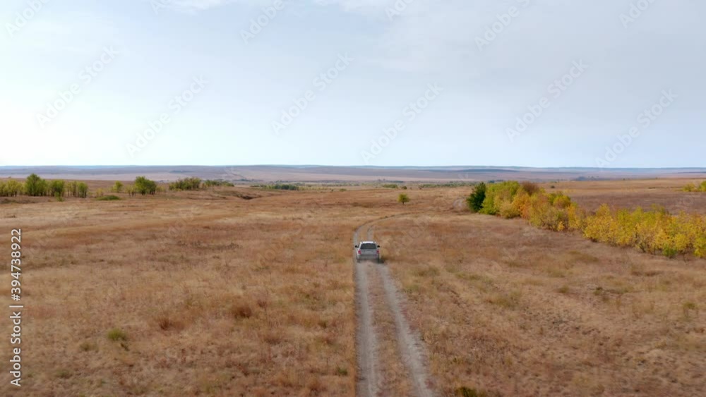 Suv off-road automobile drives slowly along empty narrow ground road stretching across dry grass meadow on sunny autumn day follow aerial bird eye view. Suv off-road automobile drives slowly along empty narrow ground road stretching across dry grass meadow on sunny autumn day follow aerial bird eye view.