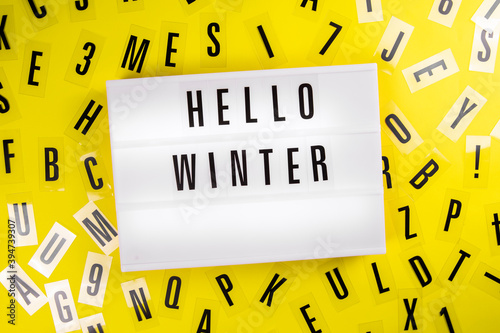 Hello Winter message on lightbox on scattered letters background of plastic alphabet. Wintertime postcard design with positive saying. holiday season slogan. Christmas and New Year's Eve concept