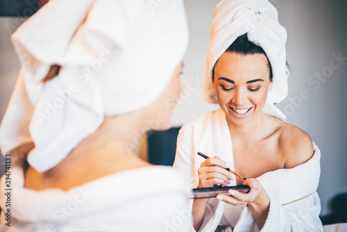 Young women wearing bathrobe sitting at hotel room, and applying makeup.