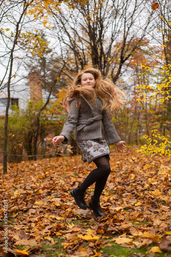 cute brunette teen girl in gray coat jumps in the autumly forest . Cosiness, autumn, fun