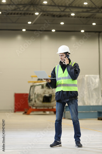 Portrait of a man , factory engineer in work clothes holding laptop and phone, controlling the work process at the helicopter manufacturer.