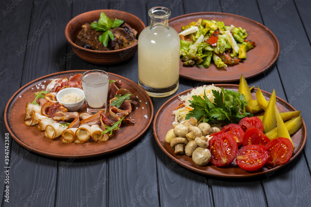 Food set with grilled pork ribs, pickled vegetables, bacon, salad, and moonshine  on black wooden background