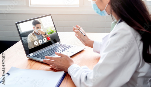 Asian doctor in an online video call with sick ill quarantine patient examining diagnosing disease viruses giving medical health advice for wellbeing  using computer laptop  wearing surgical facemask