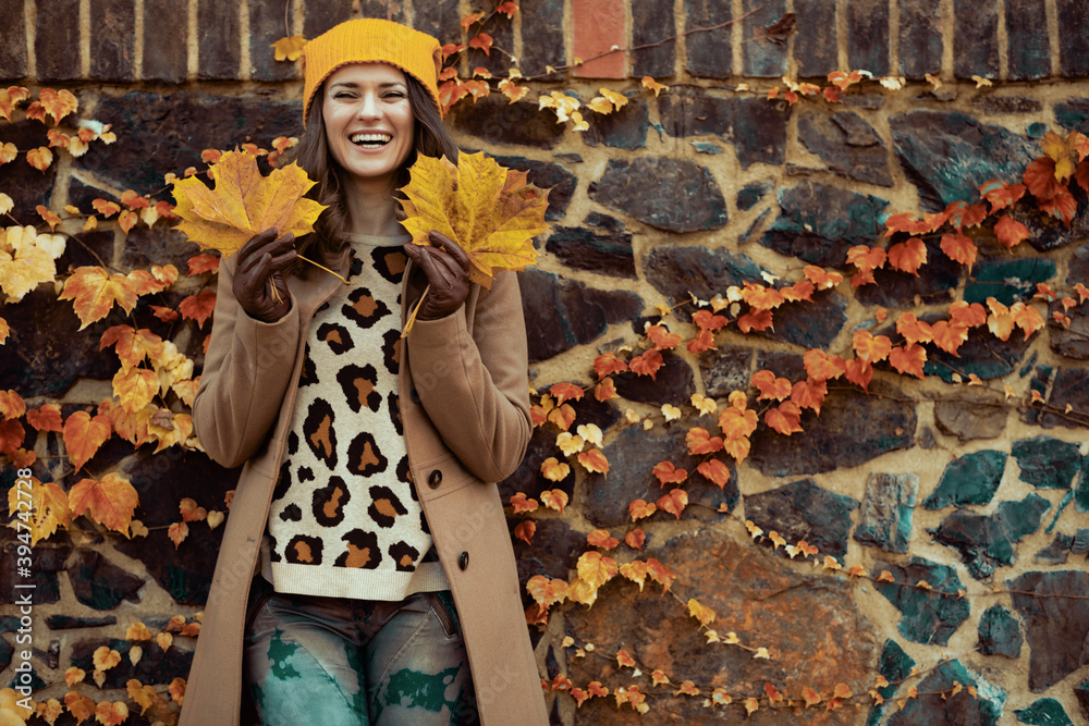 happy woman in brown coat and hat against stone wall