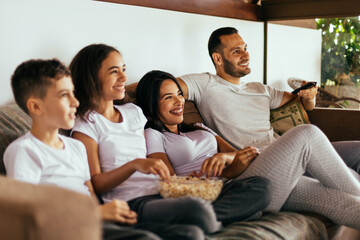 Latin family enjoying the day together at home watching tv on the couch wearing pajamas