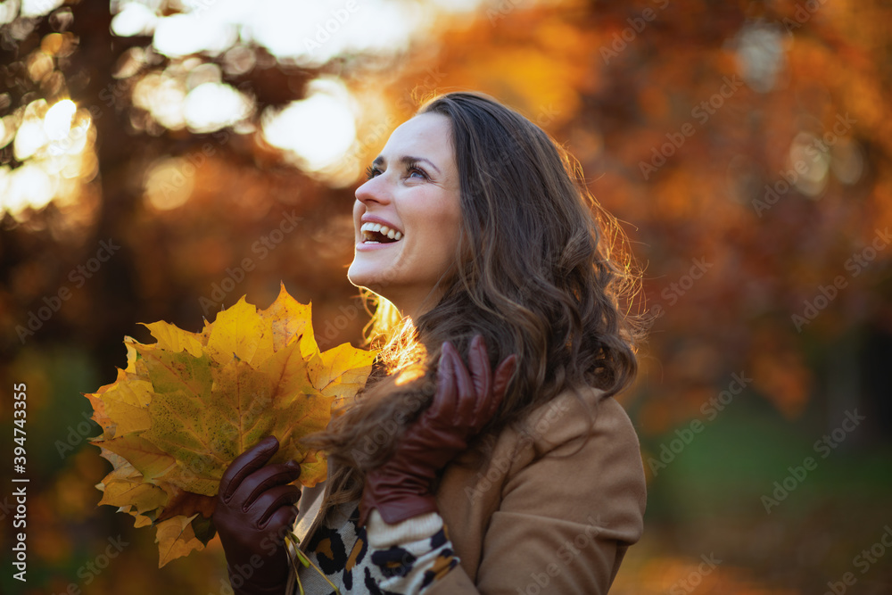 Naklejka premium smiling modern 40 years old woman in beige coat and orange hat