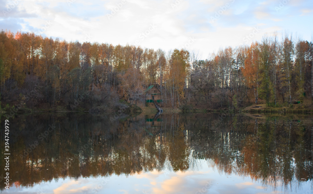 Lonely house on the lake in autumn. Autumn forest (yellow leaves) reflected on the lake