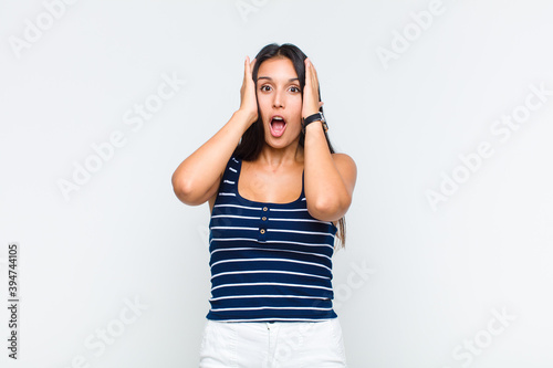 young woman looking unpleasantly shocked, scared or worried, mouth wide open and covering both ears with hands photo