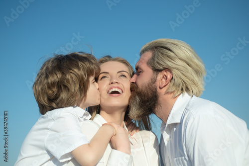 Happy family outdoors. Father and son embrace and kissing mother. Young smiling family with one child having fun together. Kids love and hug mom. Smile face. Mothers day. Parents and children.
