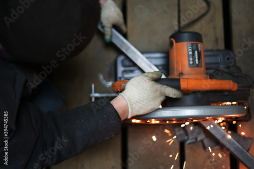 Photo of a welder's hand working cuts metal with a saw in a workshop