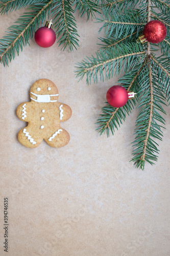 Christmas composition. Gingerbread man in a medical mask on a wooden background with red balls and a green Christmas tree.