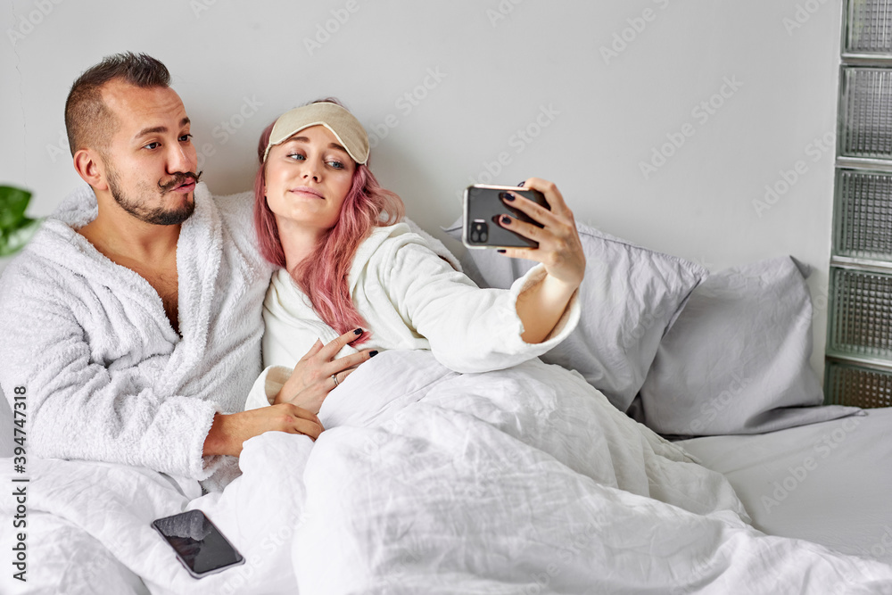 couple on bed take photo on smartphone, adorable female hold mobile phone in hands, posing at camera, have rest couple on bed take photo on smartphone, adorable female hold mobile phone in hands, posing at camera, have rest