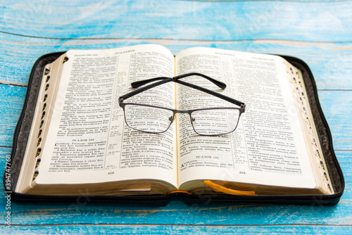 Glasses lie on the open bible, blue background. photo