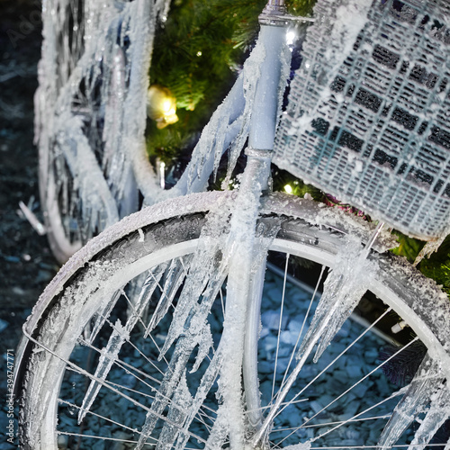 Icy bicycle wheel on the background of a Christmas tree with a garland, new year