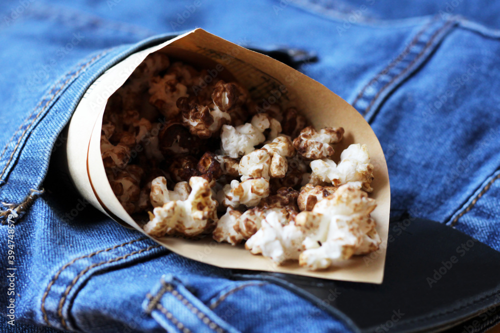 Delicious popcorn in a paper bag on a jeans Delicious popcorn in a paper bag on a jeans
