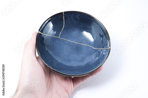 Hand holding kintsugi bowl. Gold cracks restoration on pottery restored with the antique Kintsugi restoration technique. The beauty of imperfections. representation of trauma. 