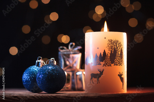 White Christmas candle, blue shiny balls and presents on a wooden table with garlands background 