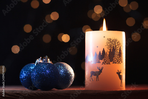 White Christmas candle and blue shiny balls  on a wooden table with garlands background 