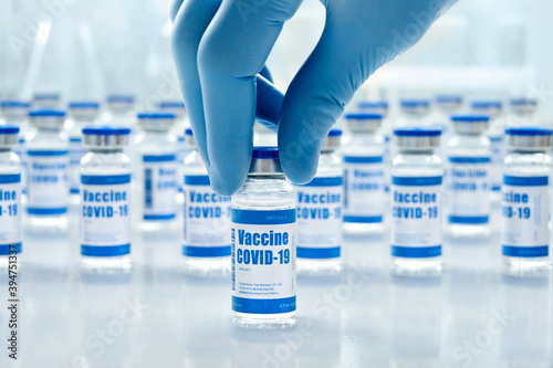 Tableau sur toile Hand of male doctor wearing medial glove holding covid 19 corona virus vaccine vial bottle for injection on medical pharmaceutical background