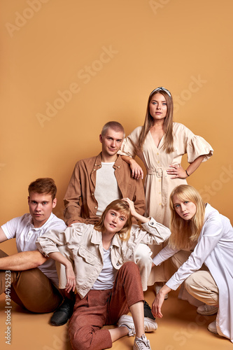 friendly group of students youth on the floor in studio on brown background, men and women in beige brown clothes posing together, as one team