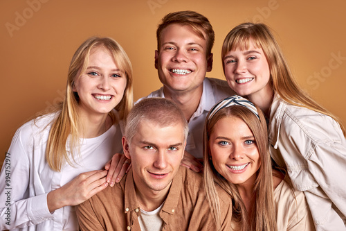 portrait of happy smiling group of youth posing together, wearing trendy coats shirts, casual clothes. friendly men and women isolated over brown studio background