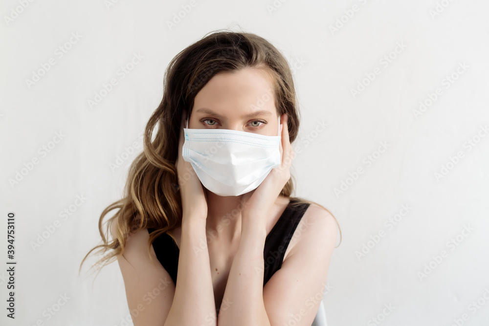 Beautiful caucasian brunette woman wearing a protective medical mask from coronavirus on her face isolated on white background
