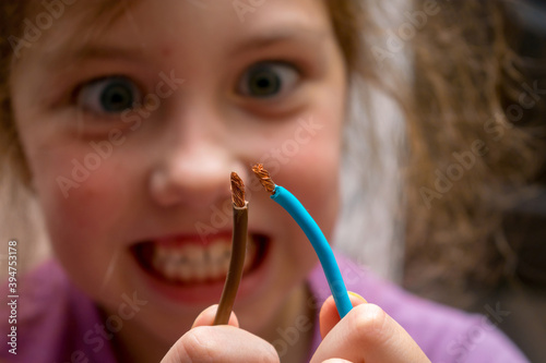 A little girl plays dangerously with electricity. The child is trying to connect two live copper wires. Selected focus.