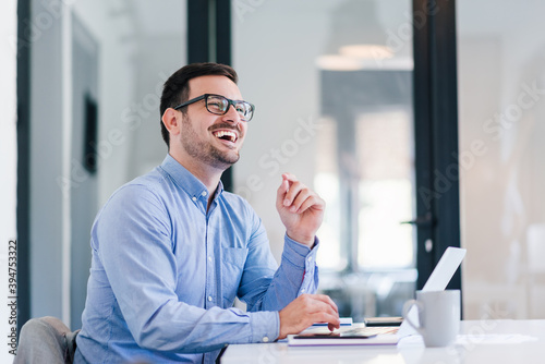 Young smiling cheerful confident businessman entrepreneur talking to satisfied customer or to colleague coworker employee while using laptop bringing good news successful closed business deal
