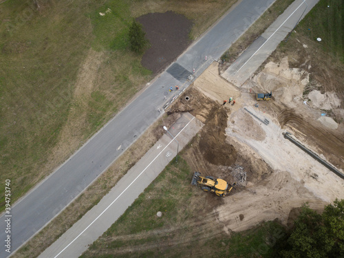 View from above of road construction works. Yellow digger and road roller. Asphalt road. Pedestrian and bicycle path.
