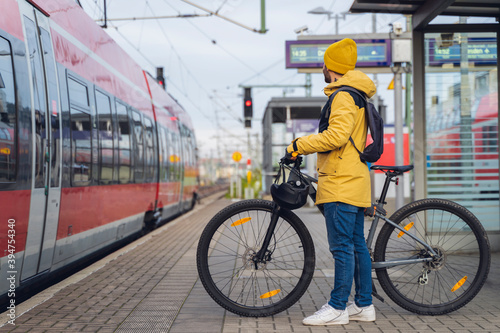 A man, wearing winter clothes, at the station, is about to get on the train, with his bicycle. photo