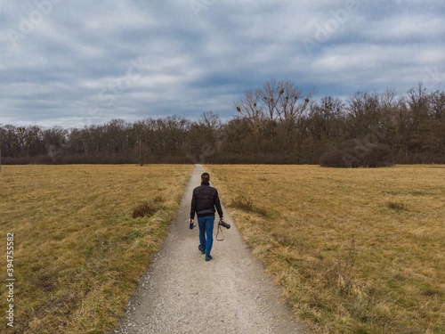 Man walk on Long path to forest between yellow fields at sunny morning