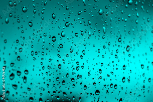 Bright fiery sunset through raindrops on window with bokeh lights. Abstract background. Water drop on the glass against the blurred silhouettes high-rise city.