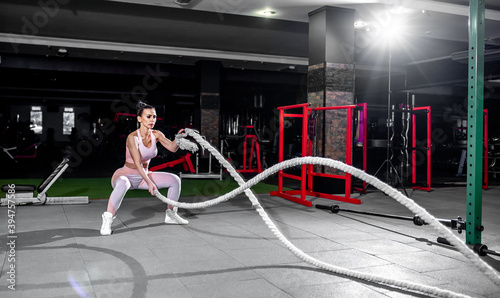 Young woman in professional gym performing exercises with combat ropes. Healthy lifestyle concept