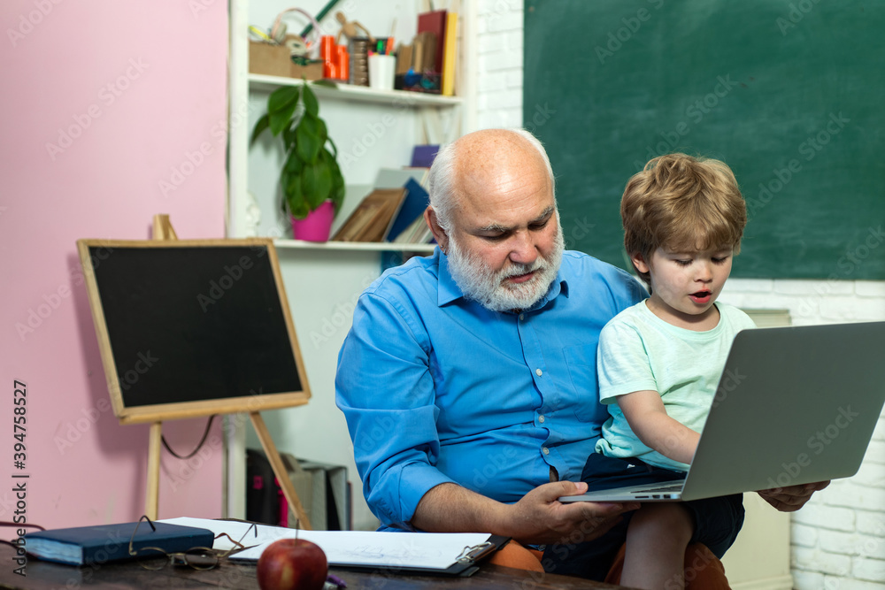 Kid with old teacher learning in class on background of blackboard - generation people concept. Portrait of grandfather and grandson on blackboard in classroom. Kid with old teacher learning in class on background of blackboard - generation people concept. Portrait of grandfather and grandson on blackboard in classroom.