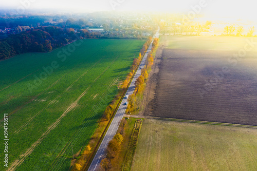 Aerial view of the road in beautiful autumn forest at sunset. Top view of perfect asphalt roadway, trees with orange foliage in fall. Colorful landscape with highway through the woodland. Travel