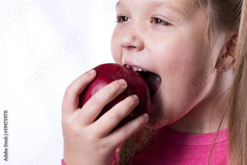 Little girl bites a red big apple on a white background, close-up