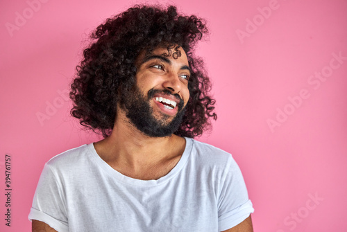 portrait of cheerful positive male of arabic appearance looking away laughing, he listen to joke, have fun with someone, isolated over pink background