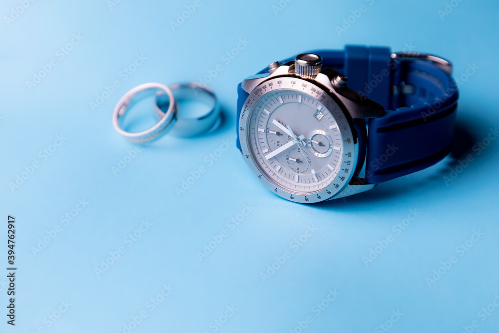 Reloj de pulsera plateado con correa azul sobre fondo azul cielo y anillos desenfocados con espacio para texto. Accesorios para hombre.