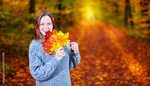 Girl with leaves in her hands in the autumn forest posing for the camera.