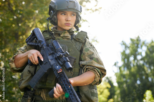portrait of confident military woman with a gun in forest, hunter female in camouflage suit with a gun stand in nature alone