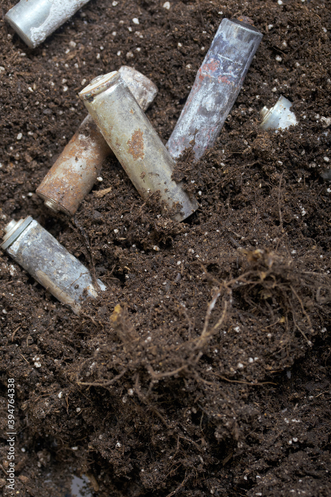 Fototapeta premium Corroded batteries covered with earth. Environmental protection and waste recycling. Close-up shot.