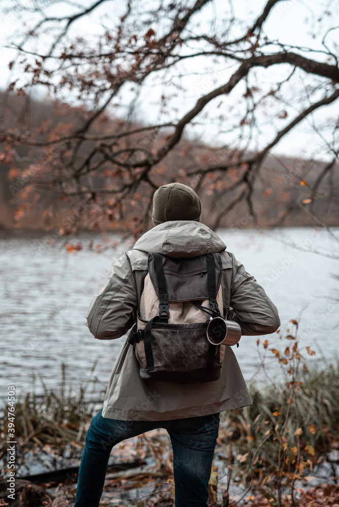 View from the back of Man holding his backpack and looking at the autumn lake view (no face)