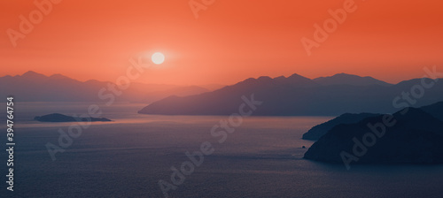 Moody sunset  the distant sun sets behind the silhouettes of blue mountains on the horizon  washed by the waters of the Mediterranean sea