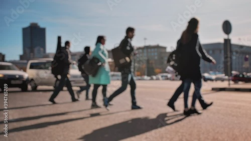 Lens blur, out of focus. A crowd of pedestrians is walking along the street with cars in the background. People walk around the big city on a sunny day. Slow motion