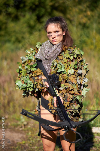 young caucasian clever woman deer hunter in green uniform with disguise and rifle in the forest, she is keen on hunting in nature, strong and fearless