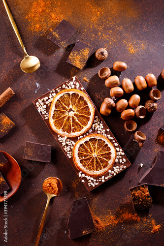 Composition of bars and pieces of different dark chocolate with orange slices, spices on a brown background close
