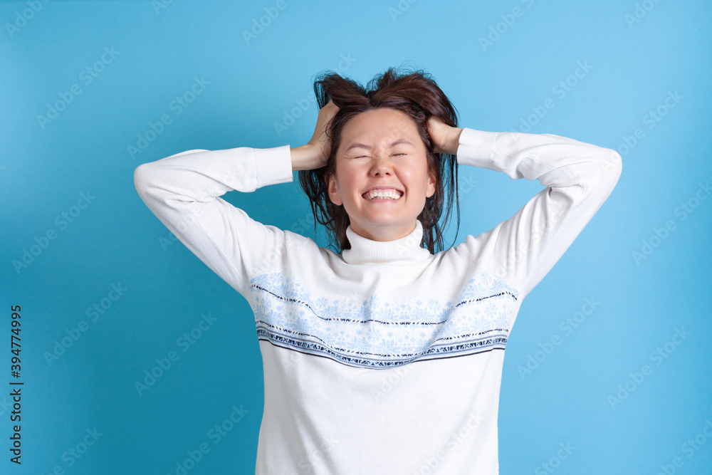 close up, laughing young Asian woman pulls her hair with her hands and closes her eyes in joy, isolated on a blue background. close up, laughing young Asian woman pulls her hair with her hands and closes her eyes in joy, isolated on a blue background.